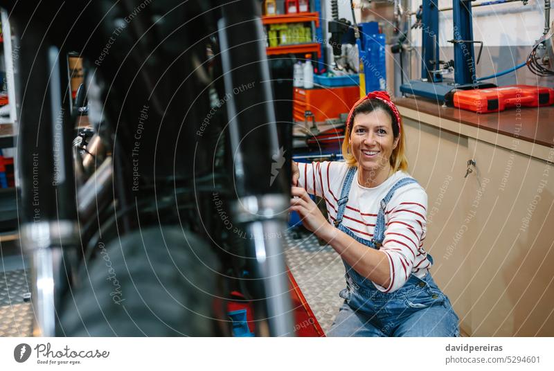 Porträt einer Mechanikerin, die ein Motorrad in einer Fabrik repariert Frau Arbeiter Sommersprossen in die Kamera schauen Blick Fotokamera arbeiten Glück