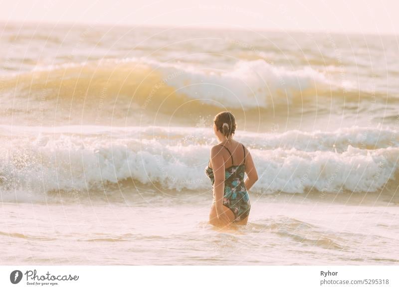 Erwachsene kaukasische Dame Frau im Badeanzug zu Fuß im Meer. Urlaub am Meer Ozean Strand. Meer Ozean Wasseroberfläche mit schäumenden Wellen. Wasser Wellen Oberfläche, krachende Wellen. Kopieren Raum. Natur Hintergrund
