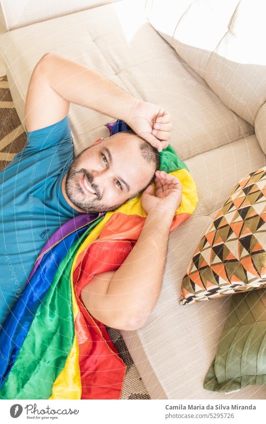Homosexuell Mann sitzt auf Sofa zu Hause mit lgbt Flagge. Weniger anzeigen Bartmann bisexuell gleich Gesicht Freiheit schwul Schwulenflagge schwule Männer