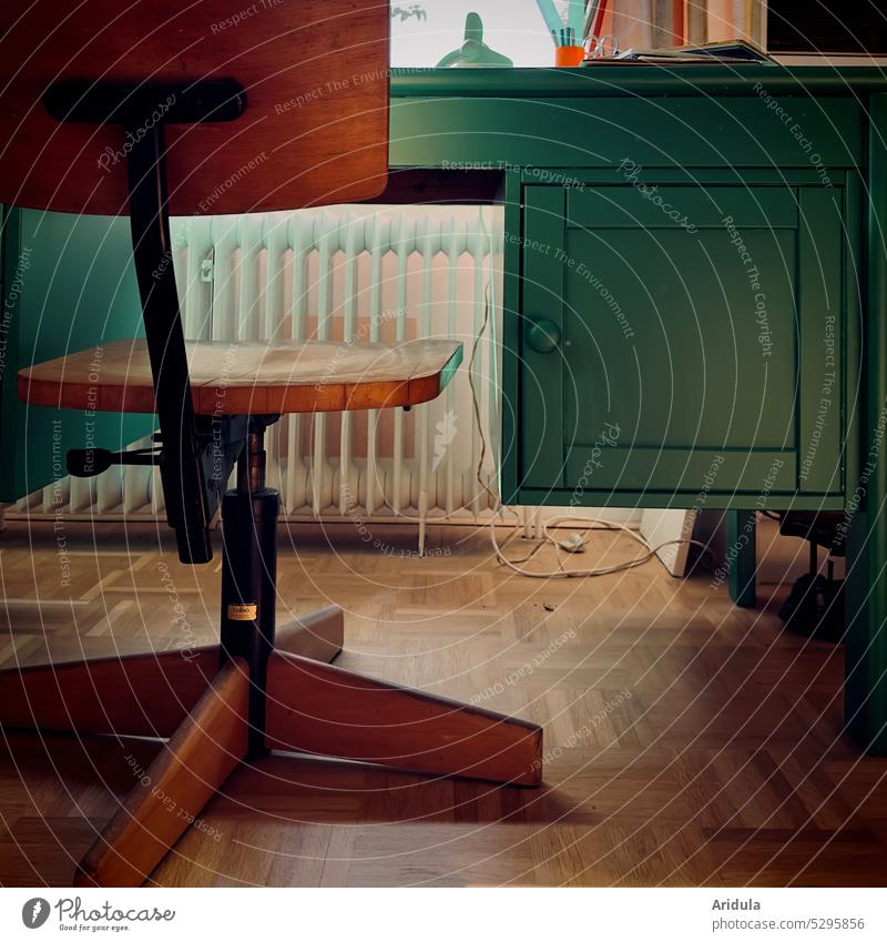 Schreibtischstuhl aus Holz, grüner Schreibtisch, Heizung, Kabel und Parkett Bodenbelag Holzfußboden Detailaufnahme Stuhl alt 70er retro Raum Möbel Licht Wohnung