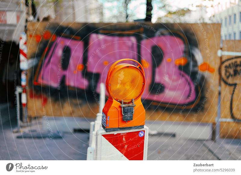Oranges Warnlicht auf Straßenbegrenzer vor rosa Graffiti auf Bauzaun orange Warntafel Straßenkunst Warnung stop anhalten Berlin Stop stoppen Zeichen Halt