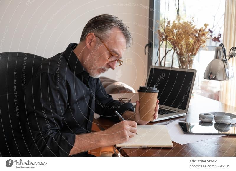 Fokussierter Freiberufler, der im Organizer am Schreibtisch im Home Office schreibt Mann freiberuflich schreiben zur Kenntnis nehmen Heimarbeitsplatz