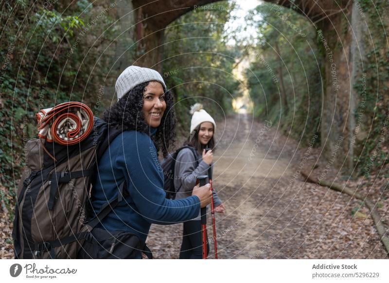 Glückliche ethnische Frau und Mädchen stehen im Wald Mutter Tochter Trekking Weg Wanderung heiter Spaziergang Lächeln Natur Wanderer schlendern Rucksack Herbst