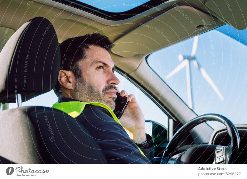 Seriöser männlicher Arbeiter, der im Auto mit seinem Smartphone spricht Mann benutzend Telefonanruf PKW Fahrzeug Wind Turbine alternativ Energie