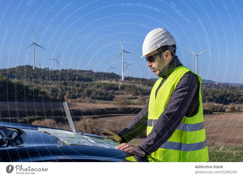 Männlicher Ingenieur, der eine Karte auf der Motorhaube eines Autos untersucht Mann untersuchen Landkarte PKW Kapuze Landschaft Arbeiter Wind Turbine Innovation