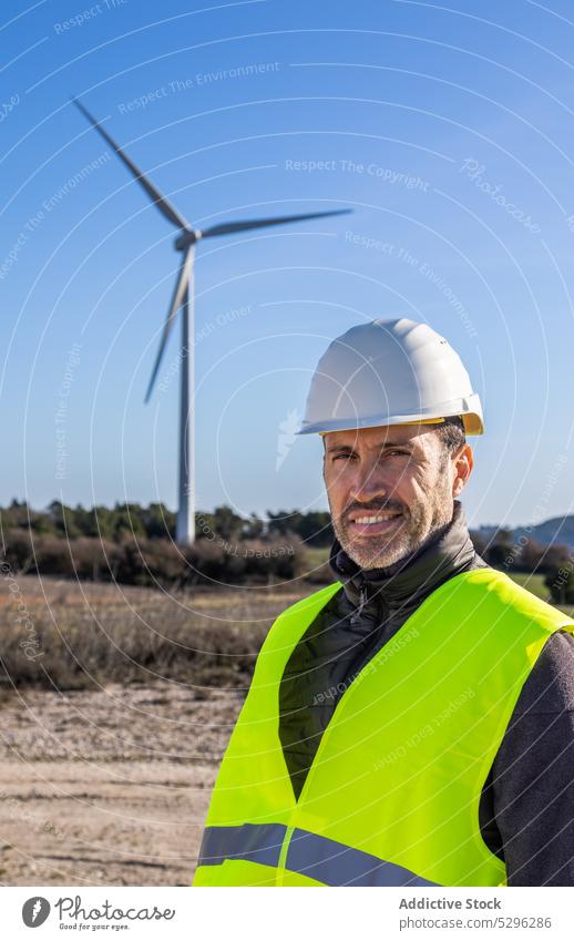 Lächelnder Ingenieur auf dem Lande vor einem Windrad Mann Turbine Arbeit Landschaft alternativ Energie umweltfreundlich Kraft positiv Wolkenloser Himmel
