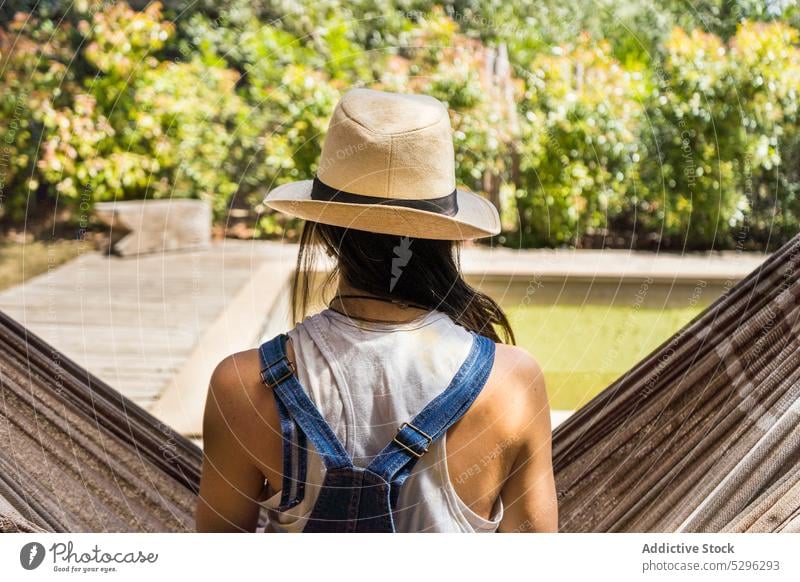 Unerkennbare Frau mit Hut ruht sich auf einer Hängematte aus Pool sich[Akk] entspannen Resort Wochenende ruhen Sommer Urlaub Feiertag Baum Sonne tagsüber