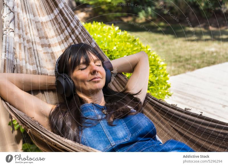Glückliche Frau hört Musik in der Hängematte im Park zuhören Kopfhörer ruhen Hof Lächeln sich[Akk] entspannen Freizeit Gesang Gerät genießen Freude lässig Audio