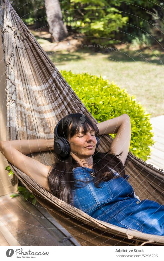 Glückliche Frau hört Musik in der Hängematte im Park zuhören Kopfhörer ruhen Hof Lächeln sich[Akk] entspannen Freizeit Gesang Gerät genießen Freude lässig Audio