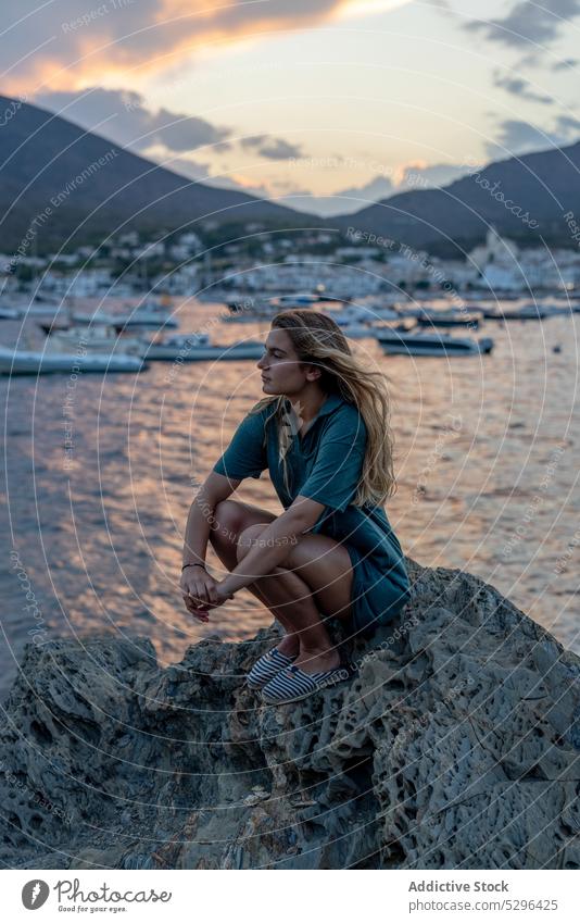Junge Frau sitzt in den Sommerferien auf einem Felsen am Meer MEER Tourist Strand Sonnenuntergang ruhen Urlaub nachdenklich Meeresufer Windstille Feiertag Küste