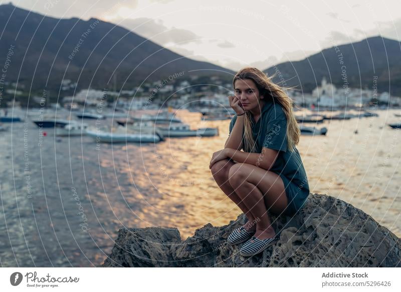 Junge Frau sitzt in den Sommerferien auf einem Felsen am Meer MEER Tourist Strand Sonnenuntergang Hand am Kinn ruhen Urlaub nachdenklich Meeresufer Windstille