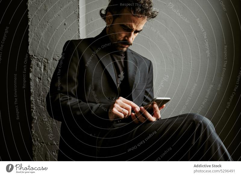 Selbstbewusster Mann, der ein Smartphone in einem dunklen Raum benutzt benutzend Browsen Apparatur Stuhl dunkel nachdenklich Vollbart Drahtlos Kavalier ernst