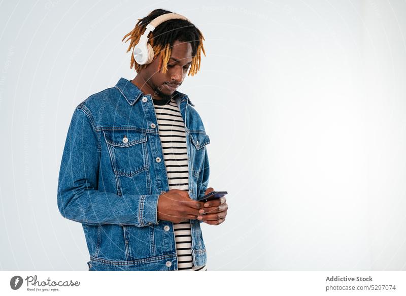Ethnischer Mann mit Kopfhörern und Smartphone Stil zuhören Musik benutzend Textnachricht Apparatur Gerät Drahtlos Nachricht modern Headset Internet Straße