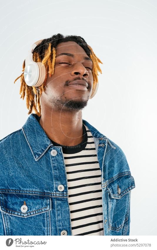 Schwarzer Mann, der mit Kopfhörern Musik hört positiv zuhören genießen Vergnügen lässig Studioaufnahme Drahtlos männlich Rastalocken Afroamerikaner ethnisch