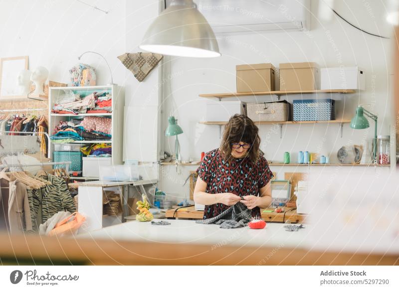 Konzentrierte Frau beim Nähen von Kleidung in einer Werkstatt Näherin Damenschneiderin Muster nähen Atelier Textil Gewebe Stoff Designer Konzentration Fokus