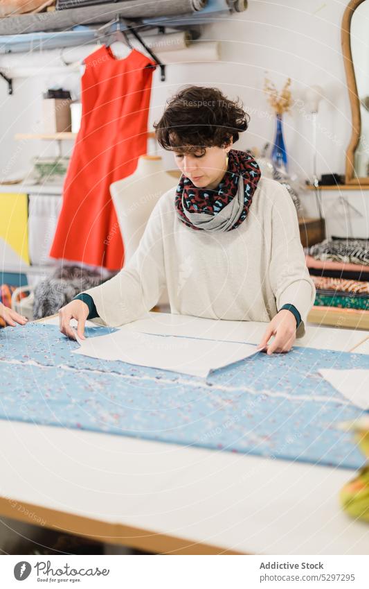 Konzentrierte Frau, die im Atelier ein Muster zum Nähen vorbereitet Näherin Designer Gewebe Damenschneiderin Stoff Werkstatt Textil Schneider kreativ Material