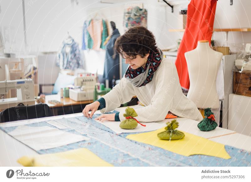 Lächelnde Designerin bei der Arbeit mit Stoff Frau Gewebe Muster Damenschneiderin Werkstatt Textil Material Atelier Handwerk Glück Näherin nähen Tisch