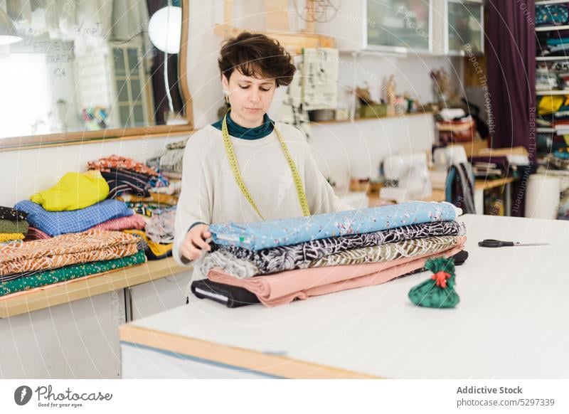 Frau mit verschiedenen Textilien in der Werkstatt Designer Damenschneiderin Atelier Gewebe messen Handwerk Klebeband kreativ Stoff Näherin professionell Arbeit