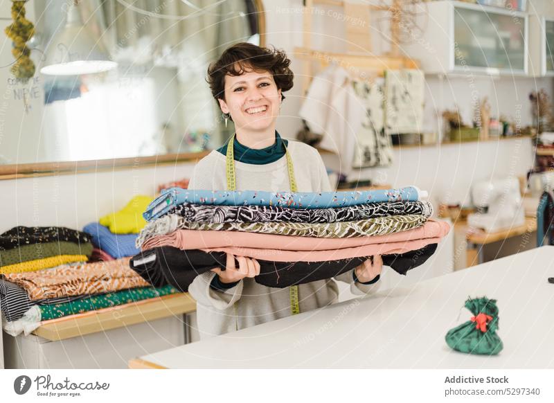 Lächelnde Frau mit verschiedenen Textilien in einer Werkstatt Designer Damenschneiderin Atelier Gewebe messen Handwerk Klebeband kreativ Stoff Näherin heiter