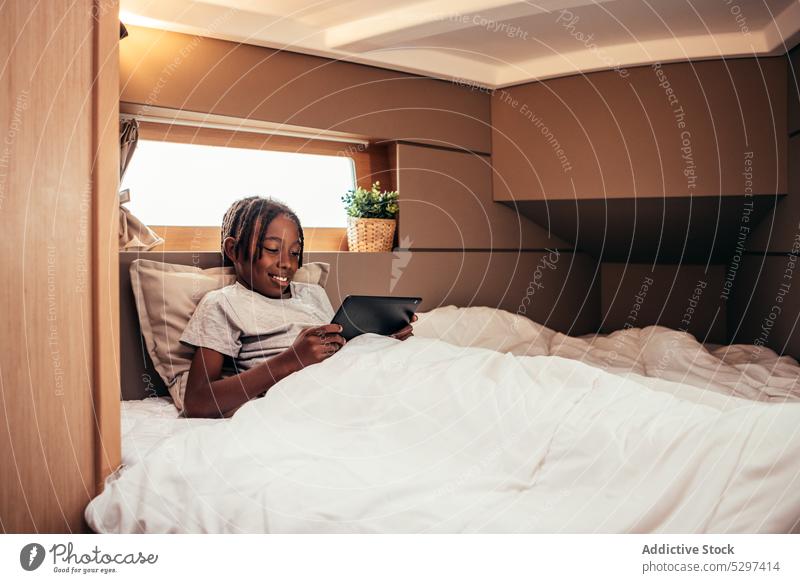 Fröhlicher schwarzer Junge surft auf einem Tablet im Bett Tablette Browsen benutzend Internet Surfen online froh Lügen Anschluss Apparatur Gerät Afroamerikaner