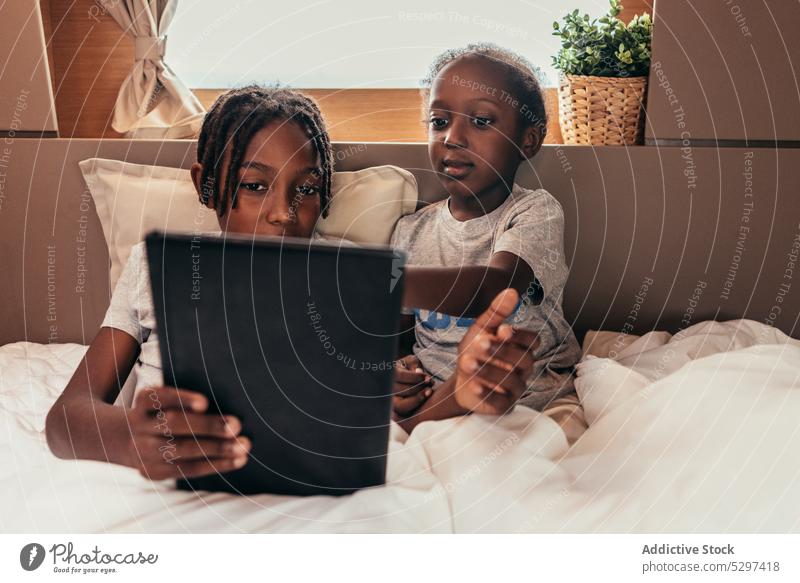 Inhalt: Afroamerikanische Kinder schauen einen Film im Bett Zusammensein Tablette zuschauen Decke ruhen benutzend Wochenende sich[Akk] entspannen Apparatur