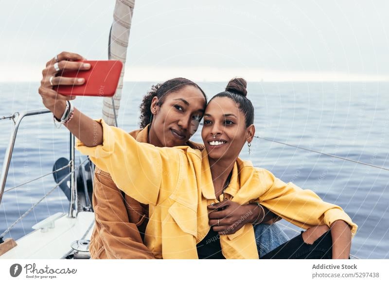 Fröhliche schwarze Freundinnen machen ein Selfie auf einer Jacht Frauen Smartphone Lächeln Umarmung Partnerschaft Zusammensein Paar Glück Umarmen ethnisch Gerät