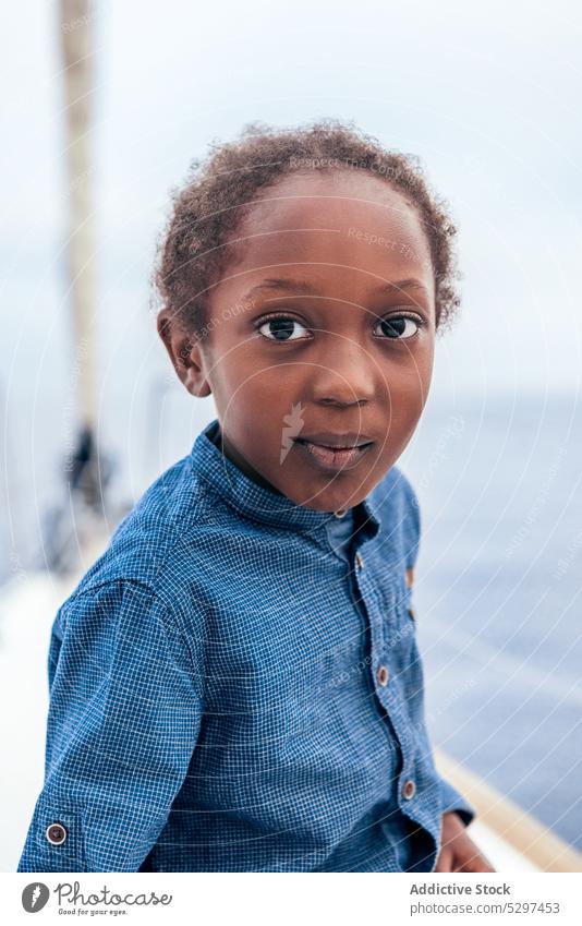 Fröhlicher schwarzer Junge lächelt und schaut in die Kamera auf einer Jacht Lächeln positiv MEER Sommer Kindheit Wasser Glück lässig Afroamerikaner heiter