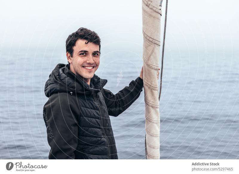 Fröhlicher Mann steht neben Segel auf Yacht MEER Wasser Jacht Lächeln Ausflug Tourist Segelboot Kreuzfahrt männlich Oberbekleidung Glück reisen Reisender Urlaub