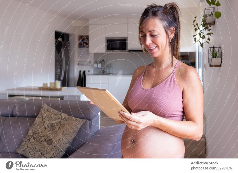 Fröhliche schwangere Frau, die im Wohnzimmer auf einem Tablet surft Tablette benutzend Lächeln Surfen online heimwärts Browsen Internet Apparatur positiv Gerät