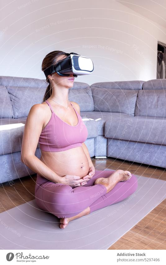 Schwangere Frau mit VR-Headset meditiert auf dem Boden Yoga meditieren Lotus-Pose padmasana heimwärts schwanger üben Virtuelle Realität Wellness Fokus