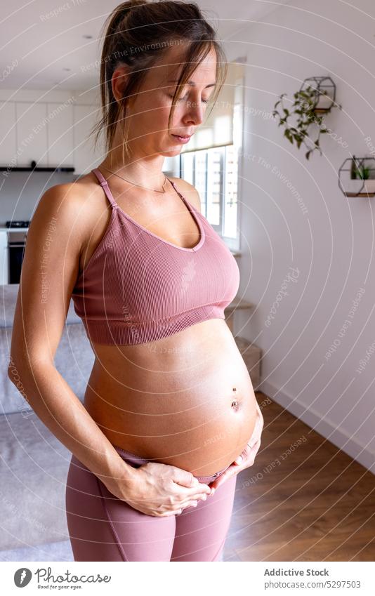 Ruhige schwangere Frau macht Atemübungen im Wohnzimmer Yoga Training Augen geschlossen meditieren Zen heimwärts Sportbekleidung Bauch berühren jung