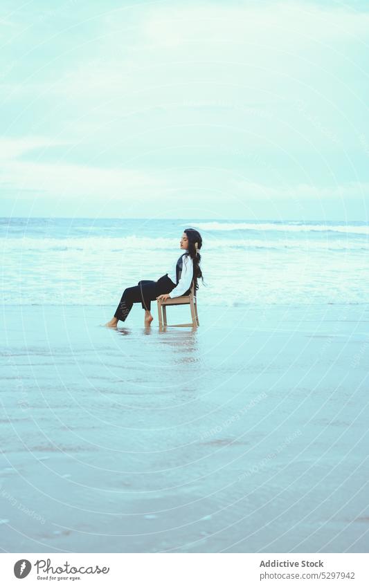 Ruhige Frau mit geschlossenen Augen auf einem Stuhl am Meer MEER Strand Meeresufer Sand Seeküste sich[Akk] entspannen ruhen Windstille Küste jung friedlich Stil