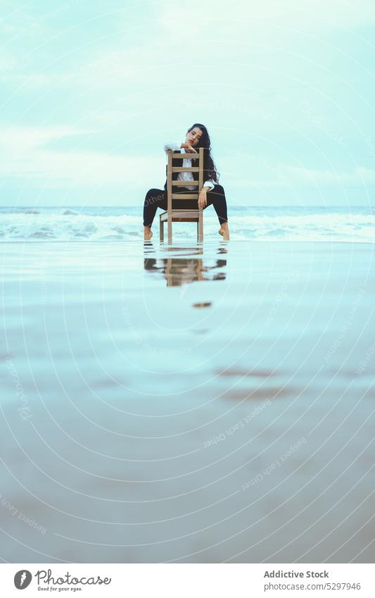 Nachdenkliche Frau lehnt auf einem Holzstuhl im Meer besinnlich Windstille MEER nachdenklich Stuhl ruhen Vorschein Porträt lange Haare jung Küste ruhig Wasser