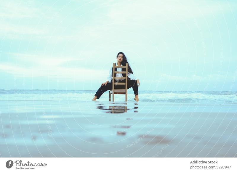 Nachdenkliche Frau sitzt auf einem Holzstuhl im Meer besinnlich Windstille MEER nachdenklich Stuhl ruhen Vorschein Porträt lange Haare jung Küste ruhig Wasser