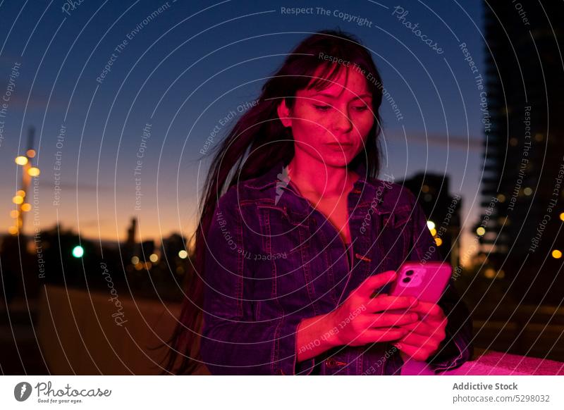 Frau benutzt Smartphone im Neonlicht auf der Straße benutzend Nacht Großstadt neonfarbig Browsen urban leuchten Apparatur Mobile Gerät dunkel Licht modern