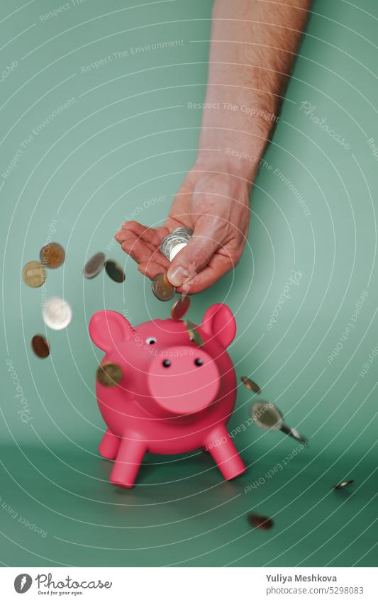 Fallende Euro-Münzen aus einer männlichen Hand und ein rosa Sparschwein auf grünem Hintergrund. Einkommen und Ausgaben in der Eurozone. Schweinchen Bank