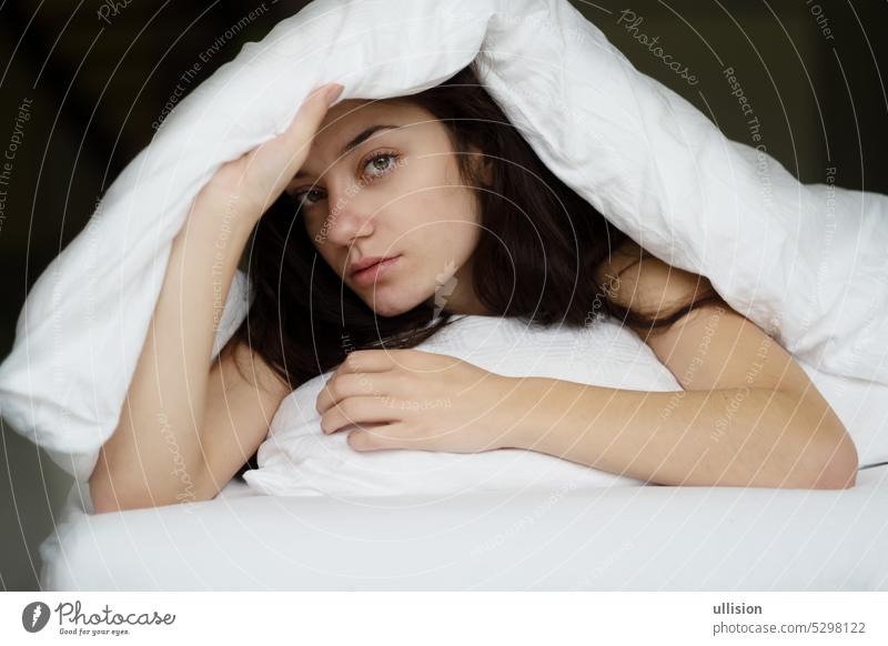 Porträt einer attraktiven, jungen, sexy brünetten Frau im Bett, Hand auf dem Kissen und Kopf unter der Bettdecke unten Decke Kopfkissen Textfreiraum