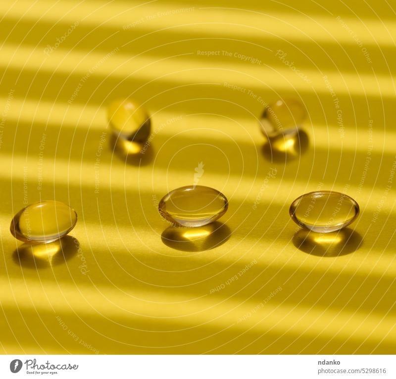 Gelbe Kapseln mit Fischöl auf gelbem Hintergrund, Nahaufnahme Schatten Erdöl Omega Pflege Omega-3 Pharma Apotheke Tablette weich Atelier Ergänzung