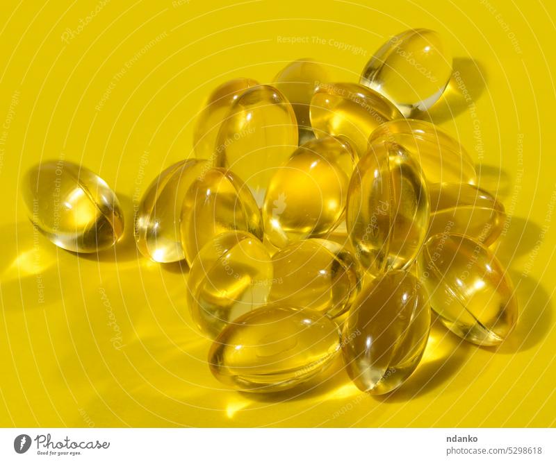 Gelbe Kapseln mit Fischöl auf gelbem Hintergrund, Nahaufnahme Erdöl Omega Omega-3 Pharma Apotheke Tablette Schatten weich Atelier Ergänzung durchscheinend