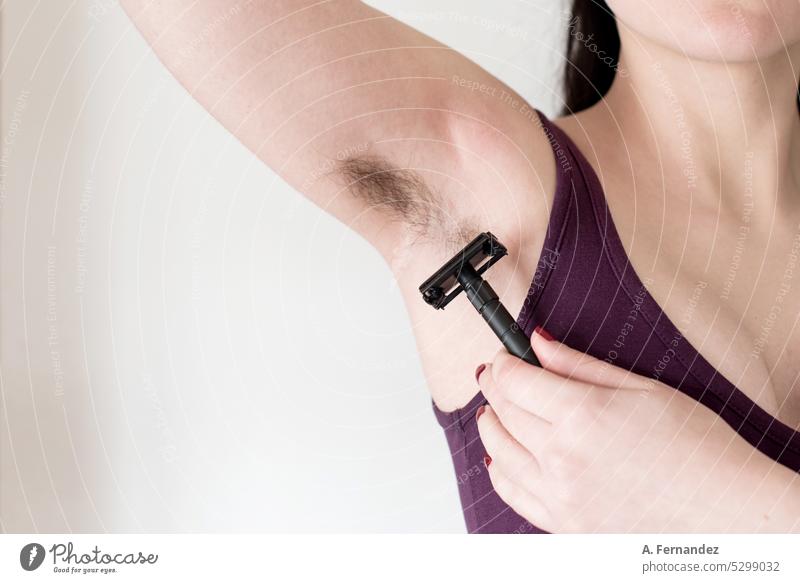 Detail einer Frau, die eine Rasierklinge benutzt, um sich die Achselhaare zu rasieren. Frau mit haariger Achselhöhle. Feminine Schönheit Kanonen Konzept Mädchen