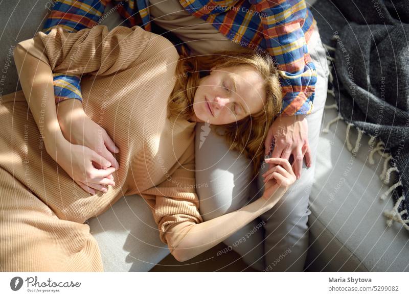 Junge schöne schwangere Frau liegt auf dem Schoß ihres Mannes. Glückliches junges Paar entspannt auf der Couch zu Hause. schlafen Mittagsschlaf Liege
