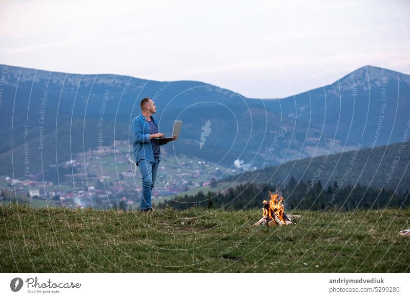 Mann arbeitet im Freien mit Laptop in den Bergen stehend. Konzept der Remote-Arbeit oder Freiberufler Lebensstil. Zelluläre Netzwerk-Breitband-Abdeckung. Internet 5G. Wanderer Tourist genießt Talblick