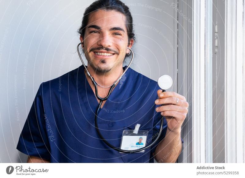 Lächelnder ethnischer Arzt zeigt Stethoskop im Krankenhaus Mann medizinisch Klinik Uniform professionell heiter freundlich Spezialist Gesundheitswesen männlich