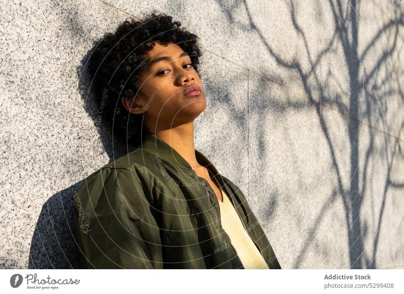 Ernster junger asiatischer Mann, der im Sonnenlicht in die Kamera schaut selbstbewusst cool Schatten Porträt gelb Vorschein Afro-Look Wand Stil ethnisch Frisur