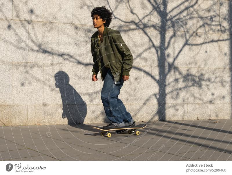 Konzentrierter ethnischer Mann fährt Skateboard auf einer Straße in der Stadt Mitfahrgelegenheit Hobby Aktivität Stil Skater Streetstyle trendy jung männlich