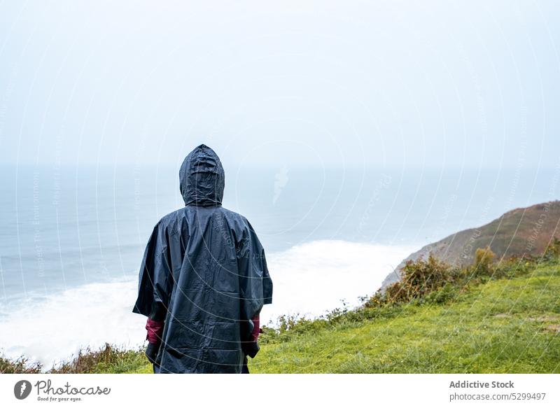 Anonymer Wanderer im Regenmantel bewundert die Meereslandschaft Frau Reisender winken Tourist MEER bewundern Natur Wanderung Unwetter stürmisch Himmel Wetter