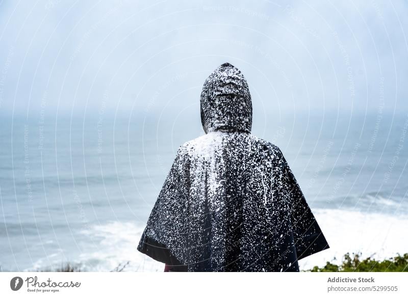 Gesichtsloser Tourist im Regenmantel mit Schnee bedeckt Reisender Kapuzenpulli Urlaub Deckung erkunden bewundern Natur Himmel stürmisch idyllisch Wetter Ausflug