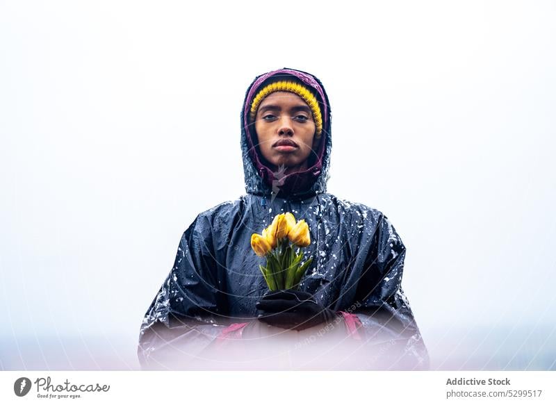 Frau im Regenmantel hält gelbe Tulpen am Meer Blume selbstbewusst Natur Blumenstrauß Saison Wetter ernst jung Windstille Dame Harmonie Individualität Umwelt