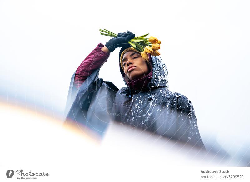Schwarze Frau im Regenmantel mit Blumenstrauß Tulpe Augen geschlossen schäumen friedlich nachdenken ernst Natur Himmel Frühling Freiheit Windstille ruhig gelb