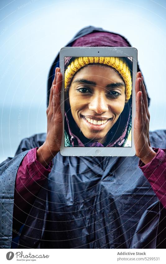 Positive Frau, die ihr Gesicht mit einem Tablet-PC vor dem Meer versteckt Reisender Wanderer Tourist heiter Tablette benutzend Deckblatt Porträt MEER